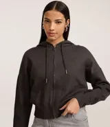 Campera corta de mujer con capucha ajustable con cordón, cierre frontal de cremallera y puños y bajo ajustados. Confeccionada en tejido de punto.