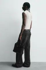 Bolso bandolera negro con detalle de cinturón, compartimento principal con cierre mediante doble imán, bolsillo interior con cierre mediante cremallera, dos asas de mano y un asa de hombro ajustable y extraíble.