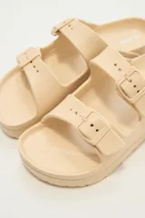 Sandalias planas color beige con doble tira y hebillas ajustables.