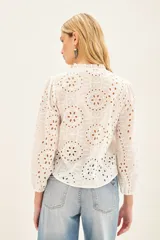 Camisa celeste de broderie de algodón con calado de hojas. Tiene cuello redondo con volados, mangas largas abullonadas con puños elásticos y cierre frontal con botones.