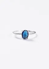Anillo de plata 925 con piedra central de zirconia azul en talla ovalada, engastada con cuatro garras. El cuerpo del anillo presenta un diseño de cintillo con pequeñas zirconias incrustadas a lo largo de la banda.