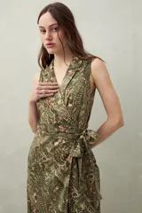 Vestido midi sin mangas con estampado floral y de hojas en tonos verde y marrón. Diseño cruzado tipo wrap con cuello sastrero y lazo ajustable en la cintura.