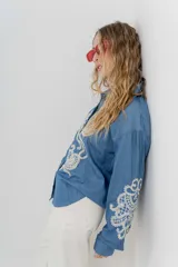 Camisa de denim azul con bordados en color crudo, de corte relaxed, manga larga y botones frontales.