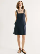 Vestido corto negro con escote cuadrado y tirantes anchos. Tiene bolsillos laterales y corte recto.