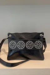 Sobre de cuero vacuno color bordó, con diseño frontal decorado con múltiples ojalillos metálicos plateados dispuestos en cuatro círculos. Cuenta con cierre superior y correa larga ajustable para llevar al hombro o cruzada.