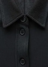 Blusa negra de manga larga con cuello camisero y cierre frontal con botones.