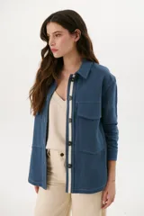 Sobrecamisa color beige de lino con cuello camisero, cierre frontal con botones negros, mangas largas con puños abotonados, dos bolsillos de parche en el pecho y dos bolsillos laterales.