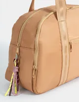Bolso color beige de tela deportiva con manijas superiores y cierre superior. Tiene un bolsillo frontal con cierre y bolsillos laterales con cierre y tiradores de cordón y goma.