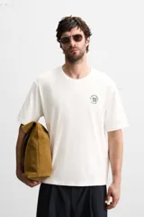Camiseta blanca de corte holgado, cuello redondo y mangas cortas. Presenta un bordado y estampado combinado en el frente.