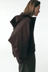 Trench corto color negro, con cuello solapa y capucha desmontable mediante botones. Manga larga tipo murciélago acabada en trabilla ajustable. Bolsillos laterales. Forro interior combinado. Cierre frontal con botones. Tejido repelente al agua.