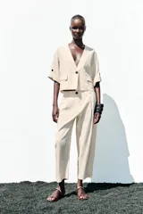 Pantalón color crema de tiro alto con pinzas delanteras y cintura elástica en la espalda. Tiene bolsillos delanteros y traseros.