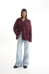 Camisa oversize color borgoña de pana con cuello camisero, cierre frontal con botones, dos bolsillos con solapa en el pecho y mangas largas con puños abotonados.