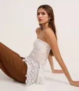 Blusa sin breteles de encaje blanco con escote recto y bajo con puntas diferenciadas.