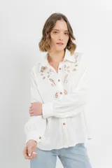 Camisa blanca de voile con bordados calados en el frente, cuello camisero, mangas largas con puños abotonados y cierre frontal con botones. 