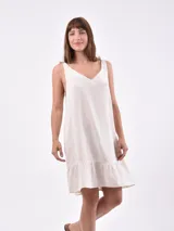 Vestido corto color crudo, de lino, con breteles finos con lazos y volado en el ruedo.