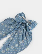 Hebilla francesa para el pelo con moño grande de tela celeste con bordado de flores blancas.