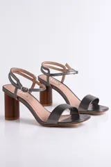 Sandalias de cuero negro con tacón cilíndrico de madera y tira fina con hebilla al tobillo.