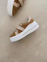 Zapatillas deportivas urbanas con capellada negra, detalles en beige y suela blanca.