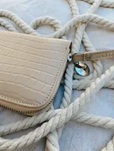 Billetera pequeña de cuero color beige con textura croco, forrada, con cierre metálico y pulsera de cuero.