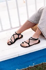 Sandalias negras de tiras finas, con suela plana y cierre con hebilla en el tobillo.