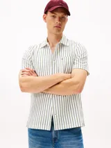 Camisa de manga corta de algodón, color blanco con rayas verticales finas en verde. Presenta cuello clásico con abertura en V y un bolsillo de parche en el pecho con logo bordado.