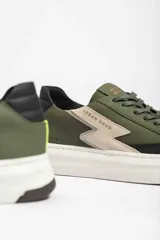 Zapatillas deportivas color verde militar con detalles en negro y beige. Presentan cordones negros, suela blanca y un rayo beige en el lateral.