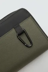 Bandolera tipo sobre color verde oliva con detalles en negro y acabado engomado. Tiene correa ajustable y extraíble, cierre de cremallera, seis ranuras para tarjetas, bolsillo interior con cremallera, dos bolsillos planos exteriores y mosquetón frontal.