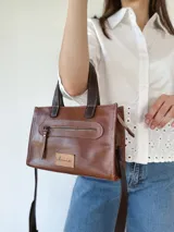 Cartera bandolera de cuero color marrón tostado, con doble asa corta y correa larga desmontable. Tiene un bolsillo frontal con cierre y un bolsillo interno.