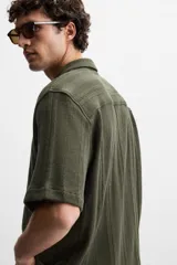 Camisa verde militar de manga corta con cuello bowling, corte relaxed fit y cierre frontal con botones.