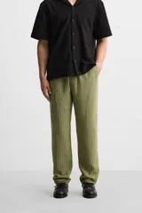 Pantalón verde oliva de corte relaxed fit, confeccionado en tejido de algodón con textura. Tiene cintura elástica ajustable con cordón, bolsillos frontales y un bolsillo trasero de parche.