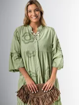 Vestido midi color verde oliva, de corte amplio, cuello mao y mangas 3/4 con volados. Presenta apliques de flores con textura en la parte superior.