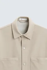 Sobrecamisa negra de tejido con elasticidad, cuello solapa y manga corta. Tiene dos bolsillos de plastrón en el pecho y cierre frontal con botones a presión.