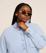 Camisa de jean de algodón, color celeste claro lavado, con cuello tradicional, manga larga y bolsillo de parche en el pecho. Presenta un cierre frontal con botones metálicos.