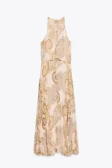 Vestido midi de cuello halter con estampado paisley en tonos beige, amarillo y marrón. Tiene lazada en la espalda, cintura elástica y falda plisada. Cierre trasero con cremallera oculta, abertura y botón.