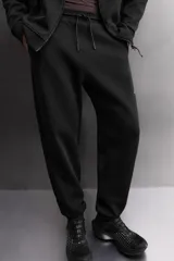 Pantalón jogger color marrón oscuro, corte regular fit, confeccionado en tejido técnico compacto de algodón con elasticidad. Cuenta con cintura elástica ajustable con cordón, bolsillos frontales y bolsillo lateral con cierre de cremallera.