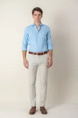 Pantalón de vestir color gris claro, de corte slim fit, con bolsillos laterales y traseros. Se ajusta a la cintura con cinturón de cuero marrón.
