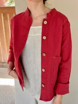 Chaqueta roja de lino y algodón, con cuello mao, cierre frontal con botones de madera, manga larga con puños arremangados, un bolsillo de parche y costuras a la vista.
