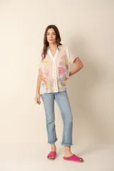 Camisa blanca de seda con bordados florales multicolor, cuello camisero y mangas cortas.