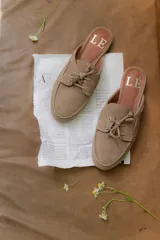 Mocasines tipo mule color beige, con detalle de cordones y ojales metálicos.