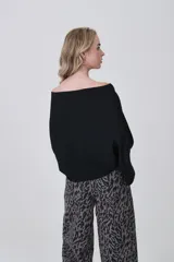 Sweater holgado de tejido ligero, color beige claro, con escote asimétrico que deja un hombro al descubierto.