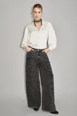 Pantalón de denim de corte ancho y tiro alto, color negro lavado, con apliques bordados florales en tonos oscuros a lo largo de las piernas.