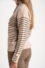 Sweater de lana y nylon, color beige jaspeado con rayas horizontales marrones oscuras. Presenta cuello alto con abertura frontal abotonada con tres botones marrones.