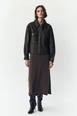 Cazadora negra de cuero con cuello solapa, manga larga con trabilla y bolsillos de parche con solapa en el delantero. Cierre frontal con cremallera y botones a presión ocultos por solapa.