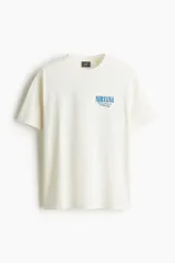 Remera color crema de corte holgado con cuello redondo y estampado frontal con el logo de la banda Nirvana y la frase 'Unplugged in New York' en color azul.