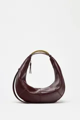 Bolso ovalado color borgoña, con asa de hombro metálica dorada y cierre de cremallera.
