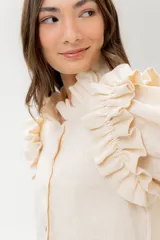 Camisa de lino color lila con volados en el cuello y en las mangas cortas abullonadas. Presenta un diseño de corte recto con cierre frontal de botones.