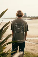 Remera verde con estampa en la espalda con texto "Glassy Waves Club" y dibujo de palmeras y una ola.