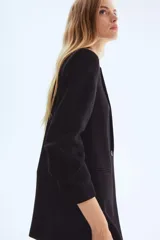 Blazer negro de corte largo y botonadura sencilla con un solo botón. Presenta solapas de muesca, bolsillos delanteros ribeteados y mangas tres cuartos con efecto remangado o fruncido.