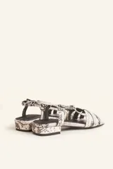 Sandalia baja de cuero charol negro con tiras entrecruzadas y pulsera al tobillo con hebilla.