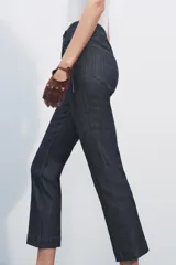 Pantalón de jean de tiro alto color negro con pierna ancha, bolsillos delanteros y traseros, y cierre frontal con cremallera y botón metálico.